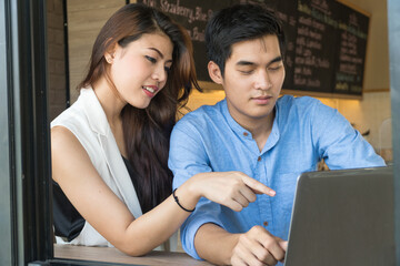 Close up Asian yong couples surfing on interne with laptop in coffee shop.