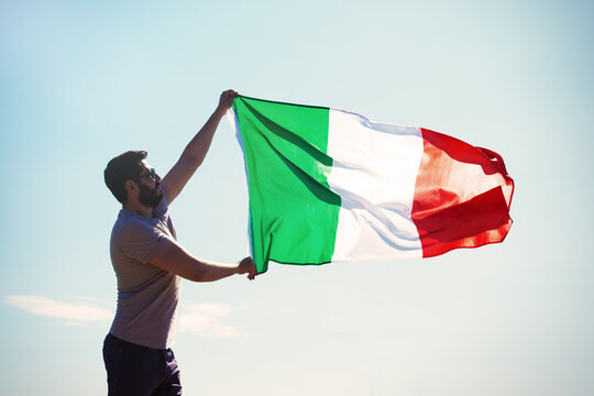 Man Holding Italian flag Against the blue sky with text Live italy Republic Day. toned image 