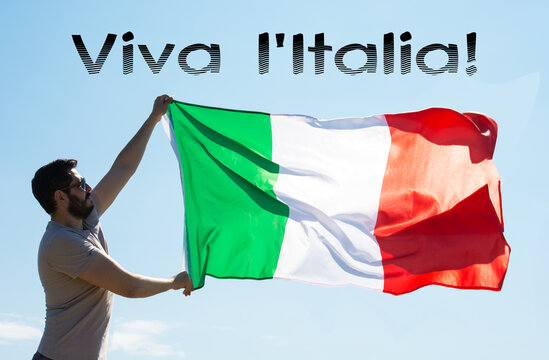 Man Holding Italian flag Against the blue sky with text Live italy Republic Day. toned image 