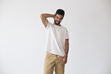 Frontal shot of attractive young hispanic man who chuckles and smiles into camera, in fashion pose in white blank simple tshirt from premium materials, cotton and vyscose