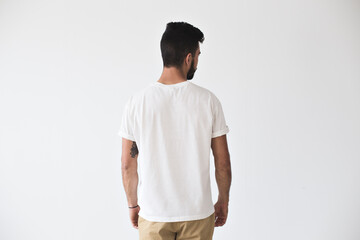 Back shot of handsome bearded man with fresh haircut and tattooed arms posing on isolated wall mockup in white simple blank tshirt ready for designs