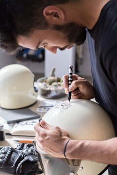 Motorcycle artist and rider, works on decorating a present to his girlfriend, personalized vintage white helmet, draws cute tiny kitten on her favourite object, helmet