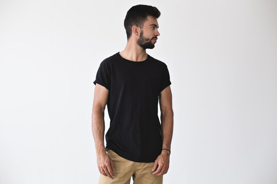 Handsome sporty strong man looks to the side, posing in studio in blank simple black t-shirt and chinos shorts on isolated white mockup