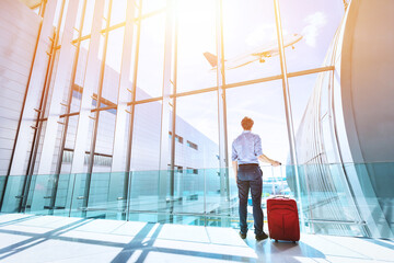 Businessman at airport terminal boarding gate looking at airplane flying