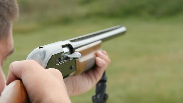 Closeup shot of a man training in competitive and recreational skeet shooting from a modern smoothbore shotgun with flying away cartridge in a green field in a sunny day in slow motion