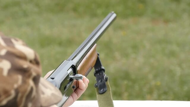 Impressive view on competitive and recreational skeet shooting from a modern smoothbore shotgun with flying away cartridge in a green field in a sunny day in slow motion.
