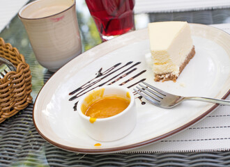 Large white dish, creamy cheesecake with mango sauce. Bright bokeh background. Basket with Cutlery,...