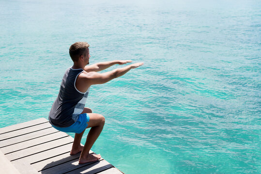 Young athlete doing squats on the sea dock. Healthy summer lifestyle.