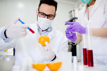 Doctor and his assistant doing GMO experiments in laboratory. Injecting chemical substances into orange.