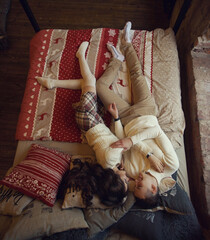 Fototapeta na wymiar Young couple staying at home together on holiday evening and lying on bed with christmas bed linen. Young lovers ib cute pullovers hugging and relaxing. Top view