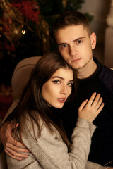 Closeup portrait of young romantic caucasioan couple sitting and higging in christmas decorated...