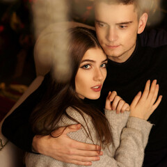 Closeup portrait of young romantic caucasioan couple sitting and higging in christmas decorated...
