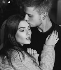 Closeup portrait of young romantic caucasioan couple sitting and higging in christmas decorated interior. Cute lovers staying at home and enjoying tome together