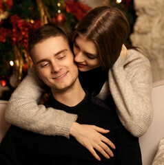 Young romantic cute couple staing at home and enjoying time together. Lovers hugging in cristmas decorated interior