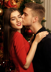 Obraz na płótnie Canvas Young romantic couple standing and hugging in christmas decorated home interior. Pretty woman in red dress and man in black