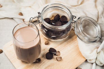 Chocolate milk with jar of cookies. Cup of cocoa on wooden board. Rustic table with grey tablecloth and white napkin 