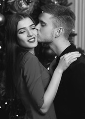 Young romantic couple standing and hugging in christmas decorated home interior. Pretty woman in red dress and man in black