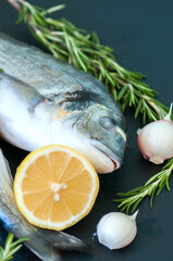 Fresh raw dorado fish with rosemary, garlic and lemon on a black slate background. Selective focus. Overhead view.