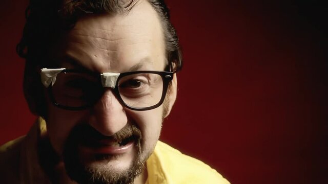 An angry ugly man wearing black broken eyeglasses (a stereotypical nerd), showing an ominous grin. Extreme close-up shot.
