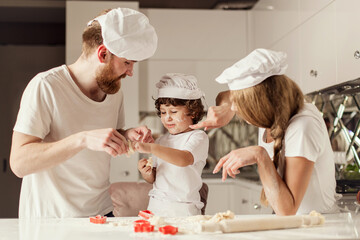 Mother, father and little son playing with the flour and red baking forms.