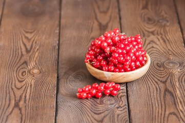 Close up of heap of fresh raw red currants in a plate on a wooden background. Copy space.