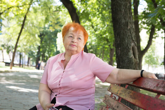 elderly woman is sitting on a bench in a city park