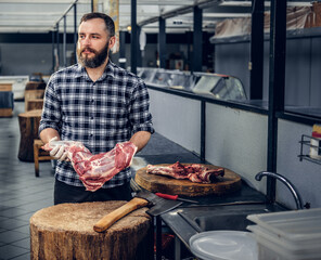 Portrait of a bearded meat man holds fresh cut meat.