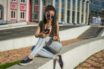 Fototapeta premium beautiful girl with zizi cornrows dreadlocks chatting on her smartphone. Urban street style
