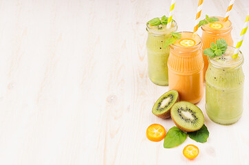 Freshly blended orange kumquat and green kiwi fruit smoothie in glass jars with straw, mint leaf, cut ripe berry, copy space. White wooden board background.