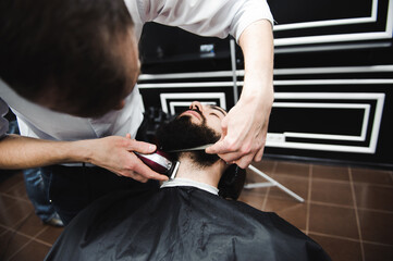 Master cuts hair and beard of men in the barbershop, hairdresser makes hairstyle for a young man