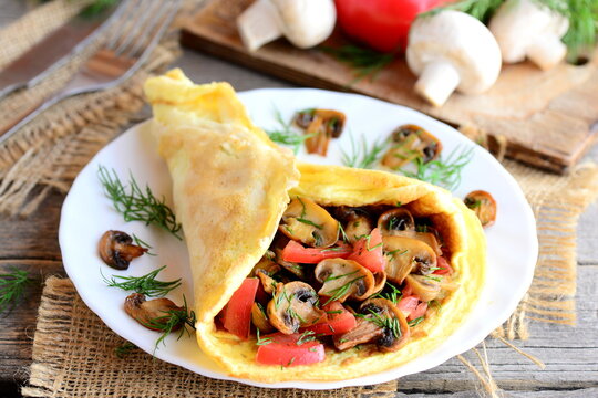 Vegetarian omelette recipe. Mushrooms omelette with tomatoes and dill on a plate. Fork, knife, fresh mushrooms, tomatoes, dill on a vintage wooden background. Easy breakfast omelette. Rustic style