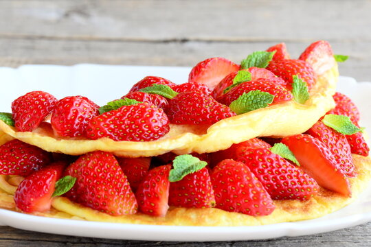 Diet filled omelette. Colorful omelette filled with fresh strawberries and garnished with mint on a plate and old wooden table. Breakfast omelette recipe. Closeup