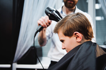 Cute little boy is getting haircut by hairdresser at the barbershop