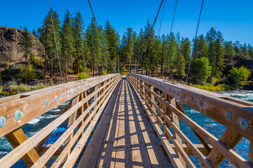Wooden bridge across the river on a background of the green forest. Dark blue Rough river. Scenic landscape. Riverside state park bridge, Spokane, Eastern Washington, USA.