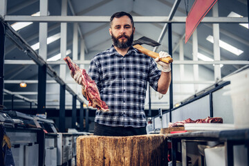 Portrait of a butcher holds an axe and fresh cut meat.