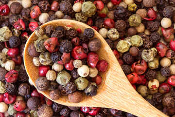 Close up mixed type of peppercorns in wooden spoon on the peppercorns background