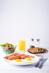 Breakfast with fried eggs and bacon with fresh salad and toast on the table.