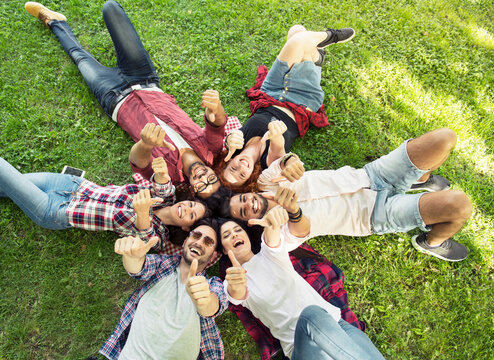 Group Of Young People Laying On The Grass In Circle, Thumbs Up, Happy