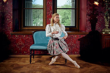 Obraz premium Young blonde ballerina in fashion clothes sitting on sofa and drinking the tea