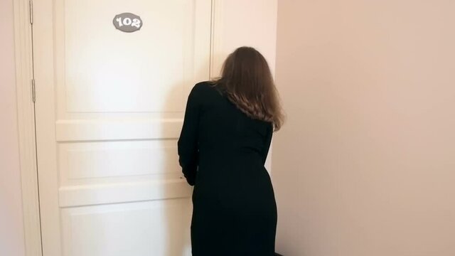 Rear view shot of young woman opens hotel room door with key
