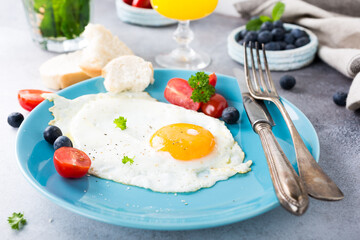 Fried egg on blue plate, tomatoes, blueberries, mint tea and orange juice. Healthy breakfast concept.