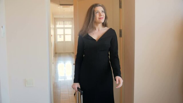 4k video of beautiful young woman in black dress opens door and walking in apartment