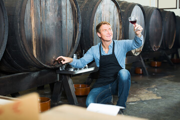 Obraz na płótnie Canvas happy seller man suggesting to try glass of wine in wine cellar