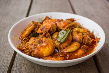 Chili prawns or know as "Sambal Udang" in a white plate over wooden background. Asian cuisine food.