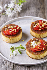 Pieces of homemade semolina cake with strawberry and pistachio decorated flowers of cherry on a rustic vintage wooden table. Selective focus 