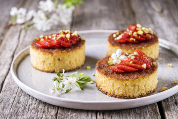Pieces of homemade semolina cake with strawberry and pistachio decorated flowers of cherry on a rustic vintage wooden table. Selective focus 