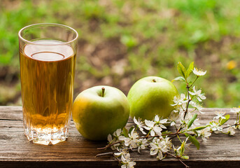 Fresh apple juice and green apples on a wooden table in the garden.