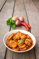 Chili prawns or know as "Sambal Udang" in a white plate over wooden background. Asian cuisine food.