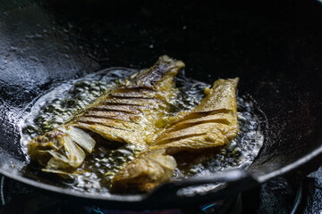 Frying fishes in black wok.