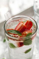 Tasty fresh cold drink with ice, water, mint and strawberry in glass. Closeup.